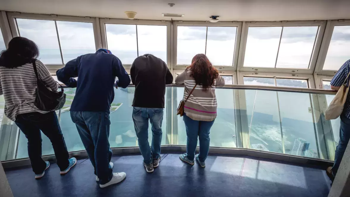 4 people leaning on the railing in the skypod looking down